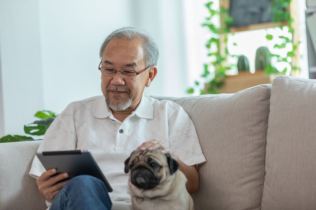 The Lodge at Stephens Lake | Senior man reading tablet on couch next to dog
